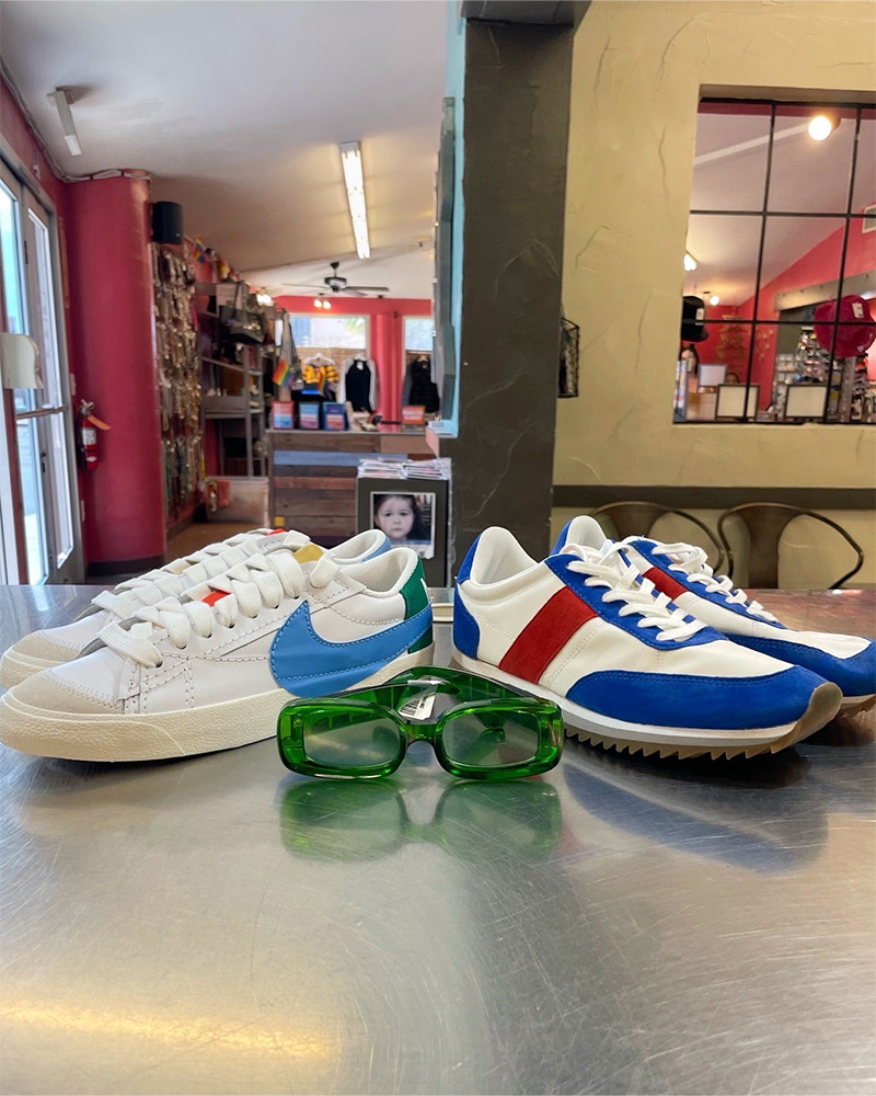 Two pairs of Nike sneakers and a pair of green sunglasses sit on top of a silver counter