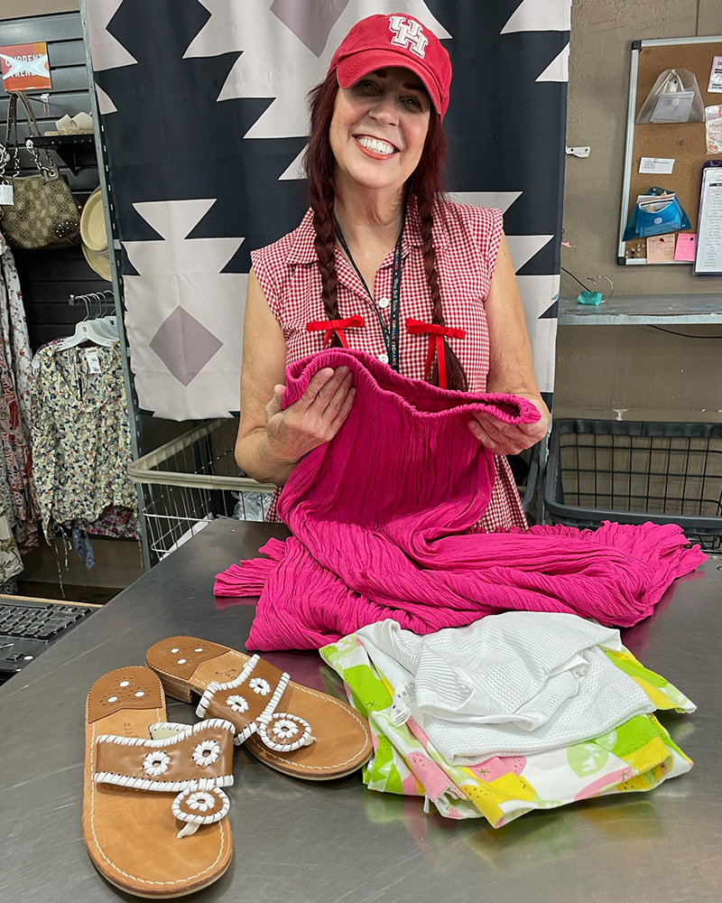 A Buffalo Exchange Buyer smiles for the camera while holding clothing behind a counter