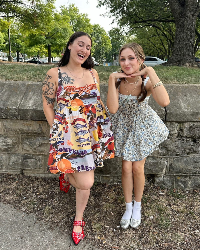 Two women stand outside in a park wearing patterned sundresses