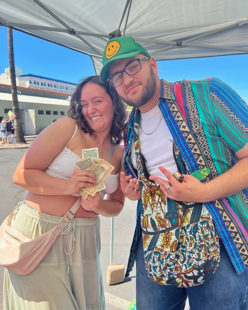 a couple pose holding dollar bills while standing under a pop up tent