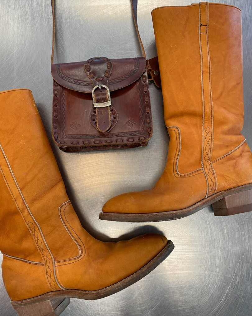 Flat lay of vintage western boots in tan leather with a mini tooled leather crossbody purse at the Buffalo Exchange buy counter