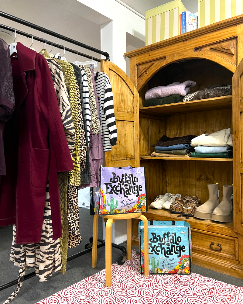 An organized closet with a rack of clothing and open armoire 