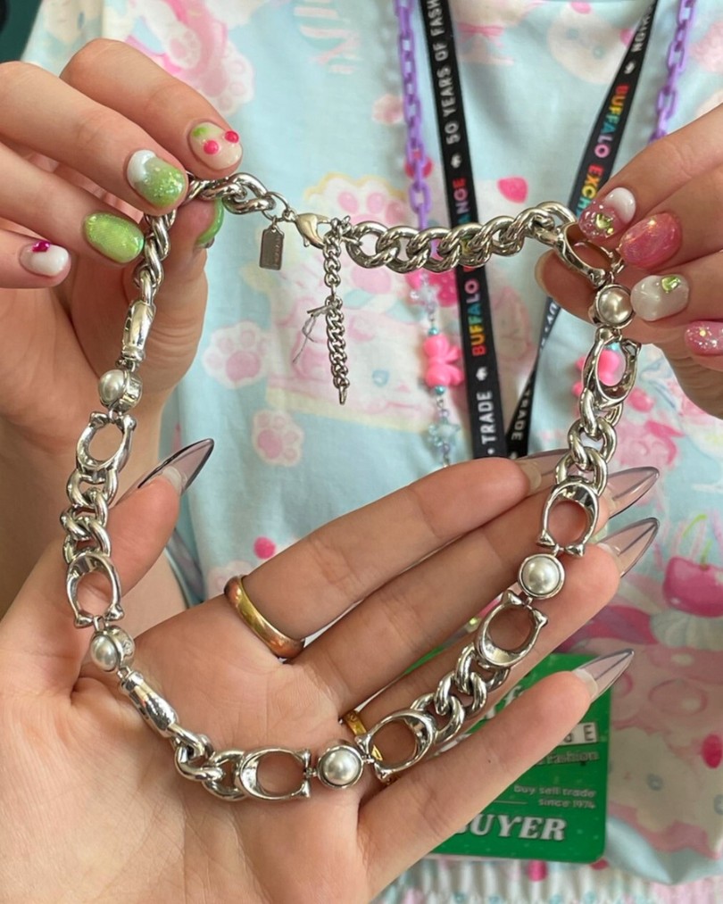 The hands of a Buffalo Exchange buyer with a cherry-inspired manicure holding up a Coach curb chain necklace with sterling silver links and pearl accents